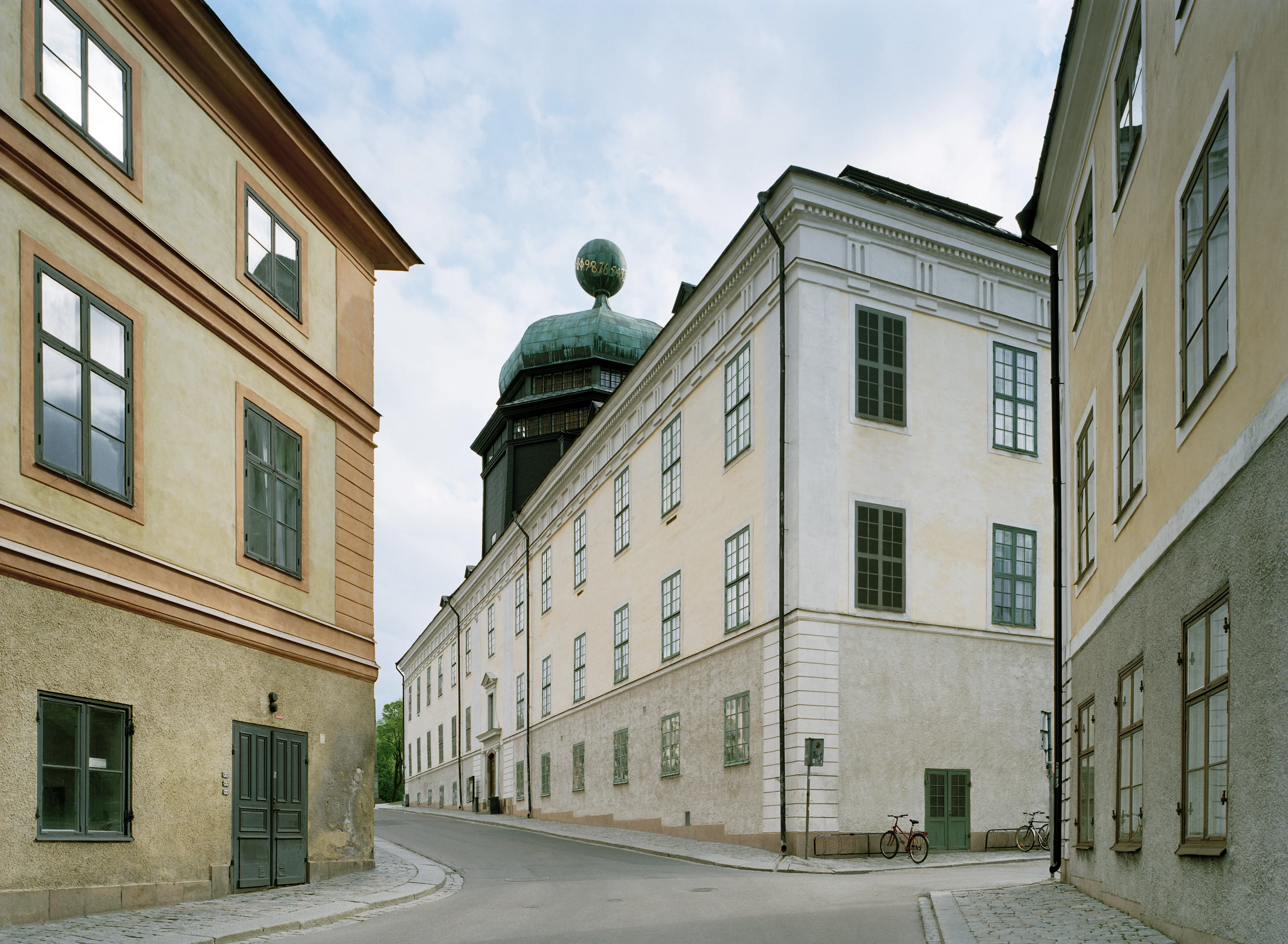 Gustavianum. En gulputsad, klassicistisk byggnad i två våningar. På taket står en åttakantig påbyggnad med kupoltak.
