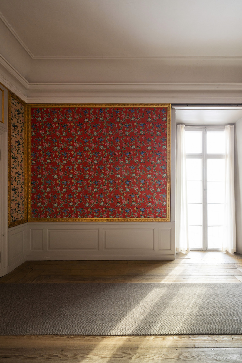 Dagsljus strömmar in genom en glasdörr i ett rum med röda. blommiga tapeter.