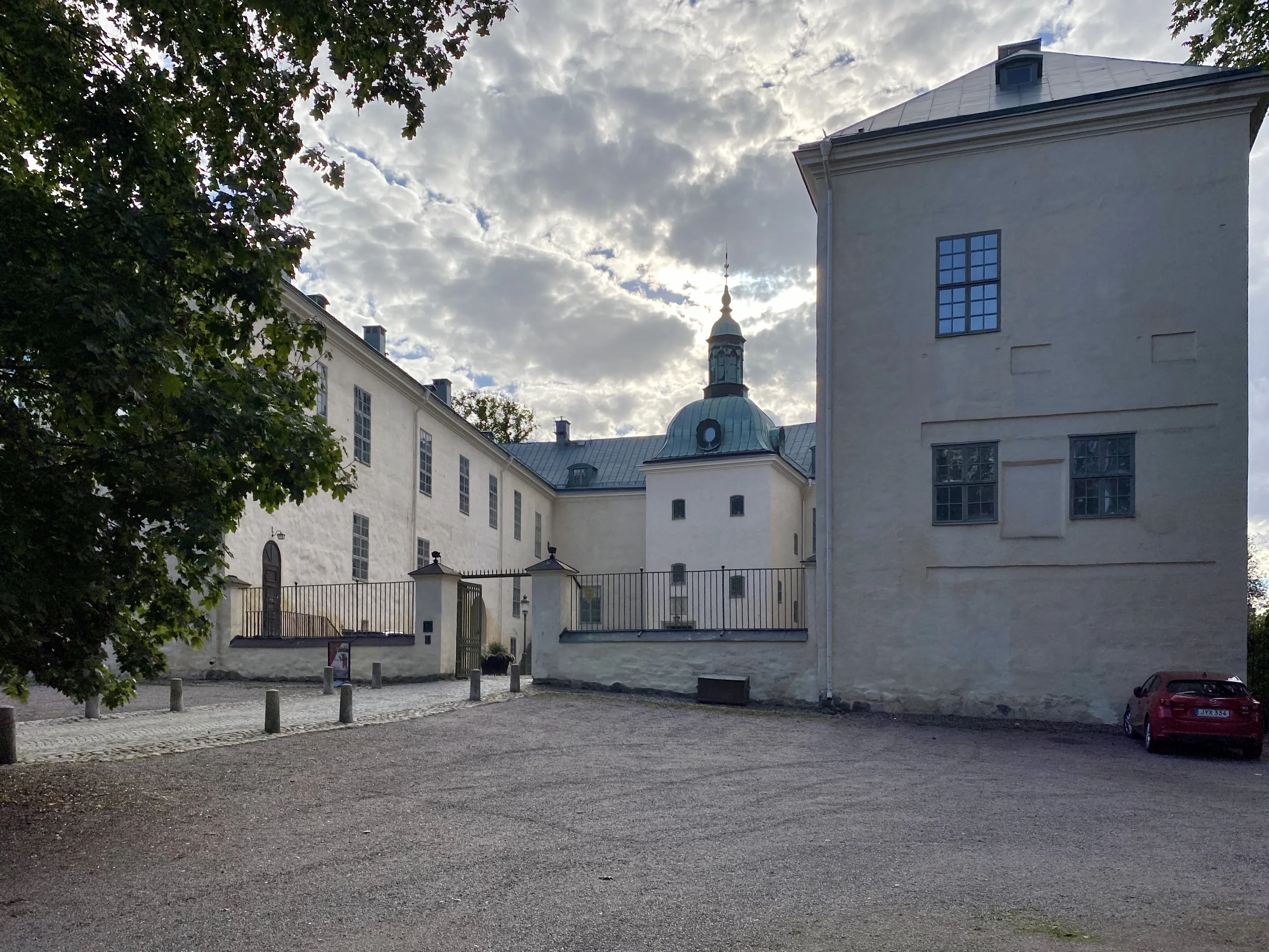 Linköpings slott, fasaden mot torget. En vitputsad tvåvåningsbyggnad med mitt-torn och stora flyglar. Sommar och grönska