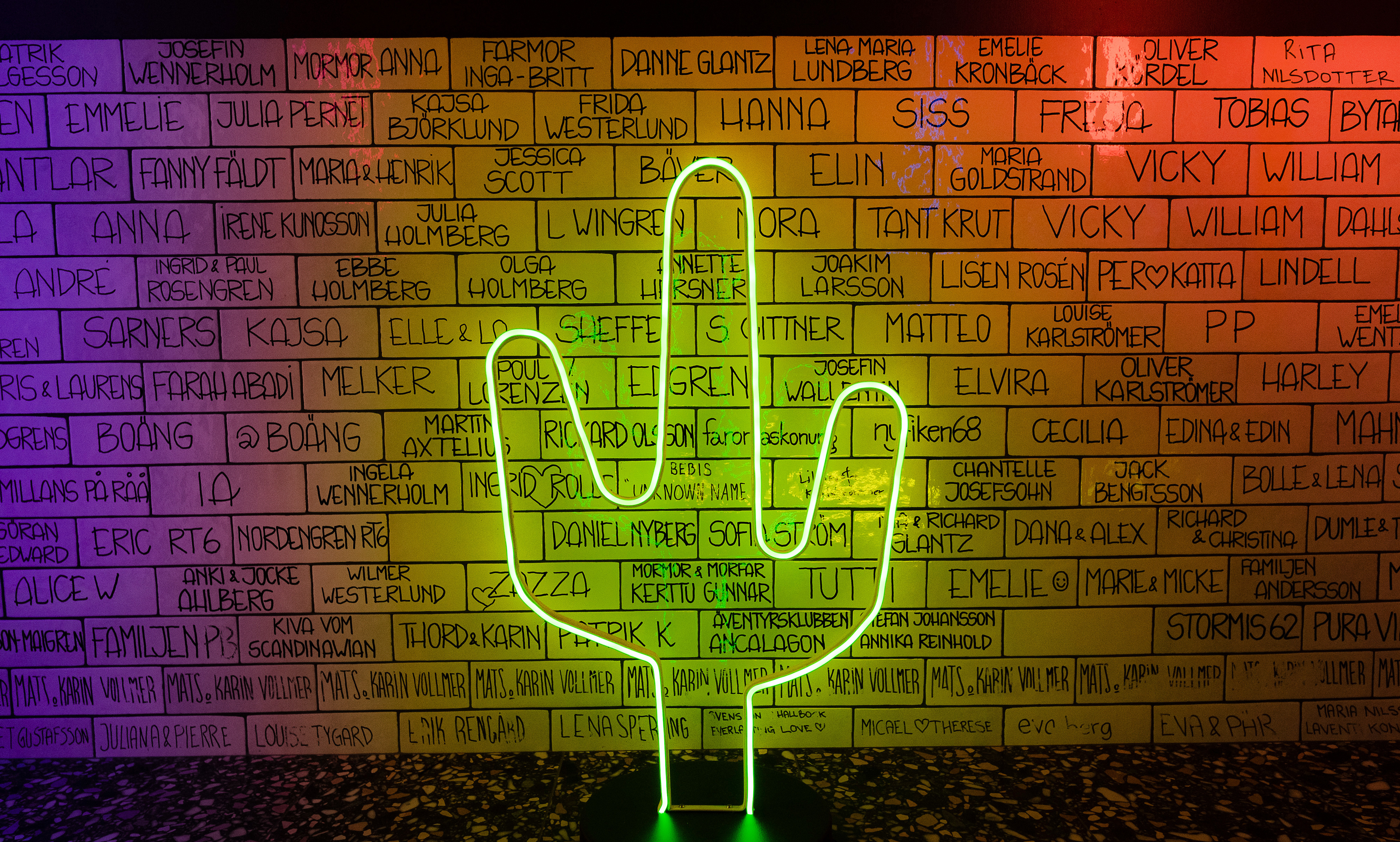 Neonkaktus framför väggen med namngraverade kakelplattor.