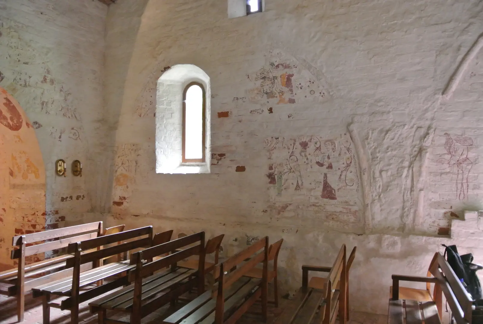 Kyrkans interiör med träbänkar och väggmålningar.