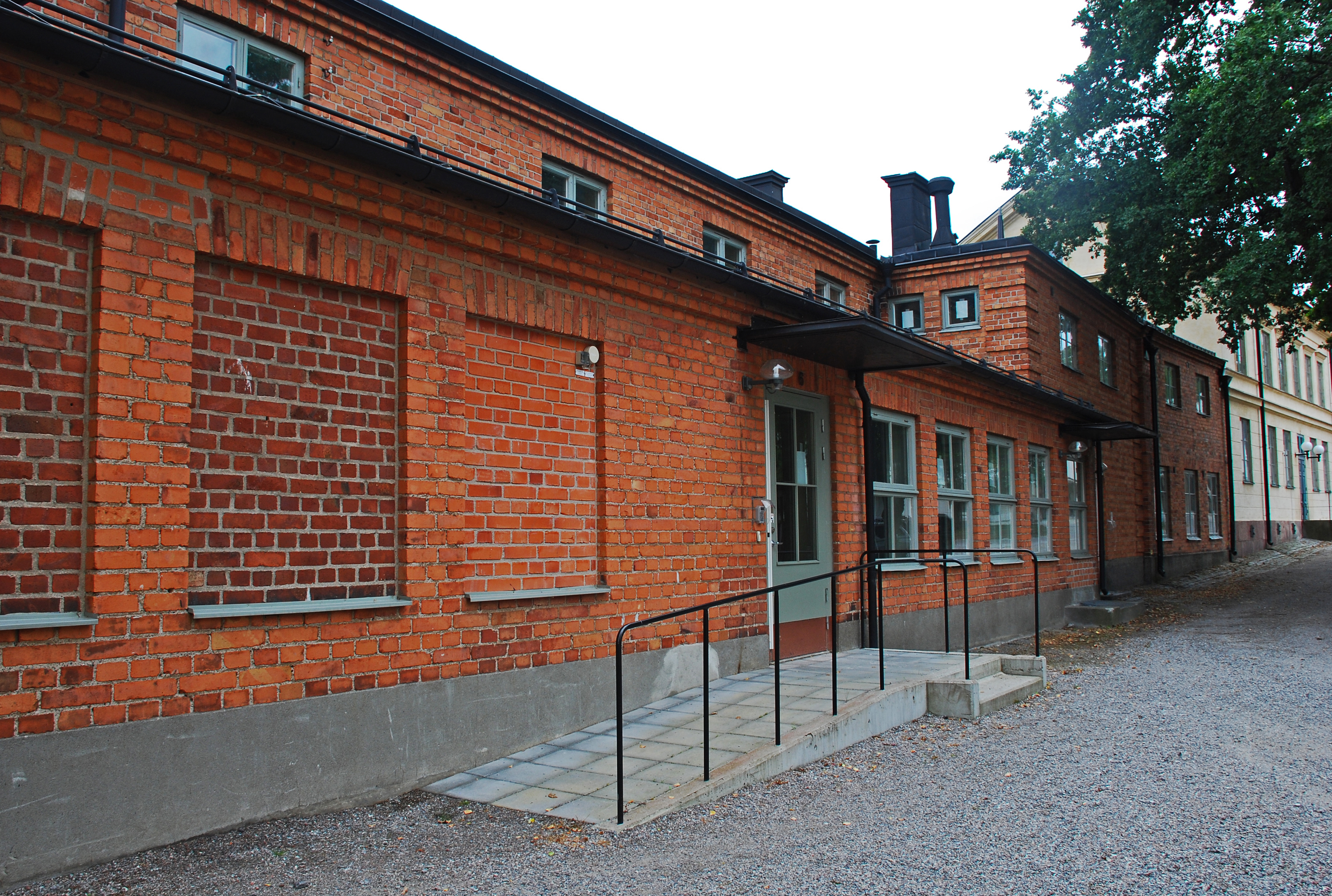 Byggnadsdepartementet, Skeppsholmen. Låg tegelbyggnad. Entrén med rullstolsramp.