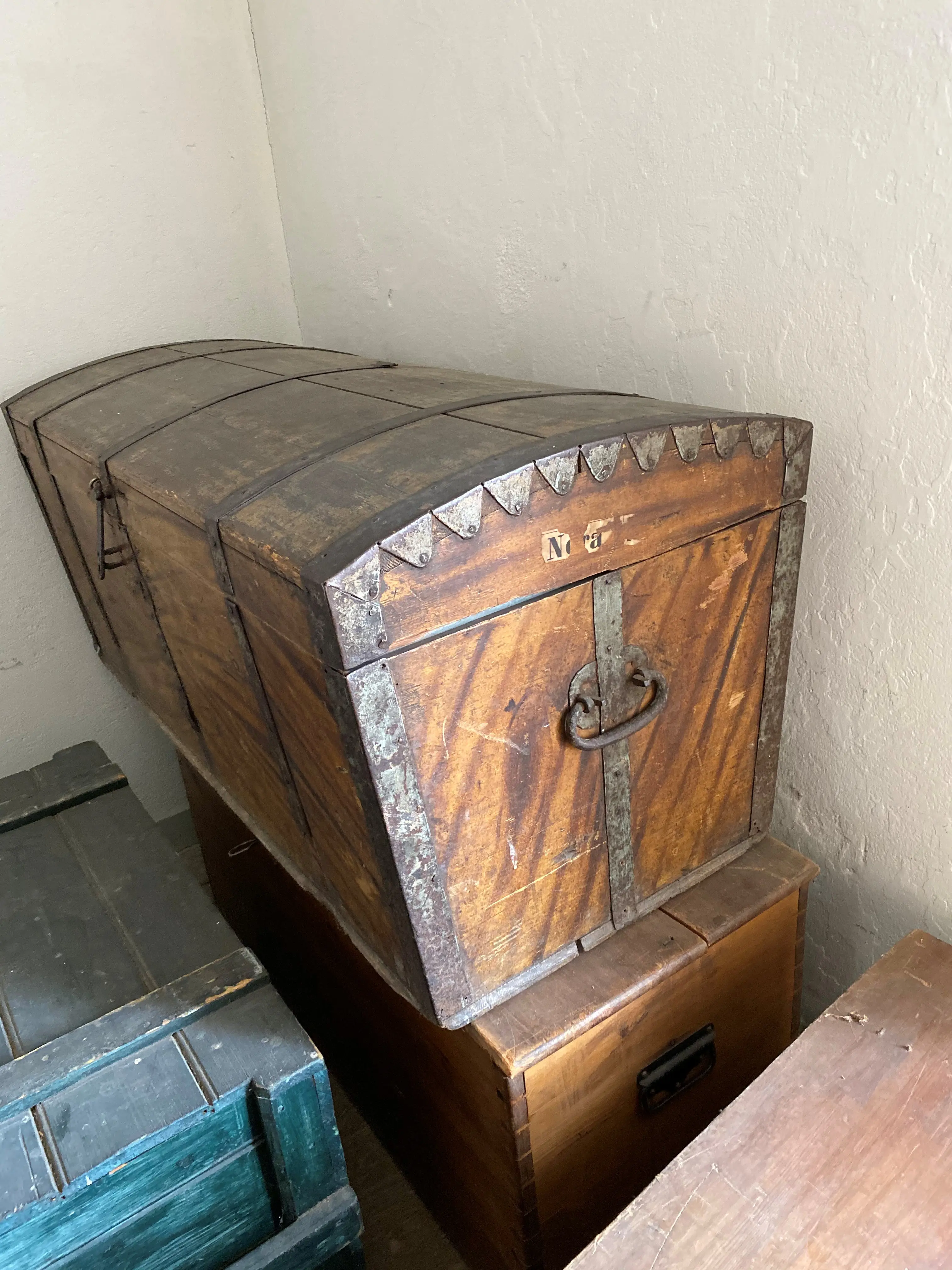 Två träfärgade kistor staplade på varandra. Till vänster i bild en blågrön trälåda.