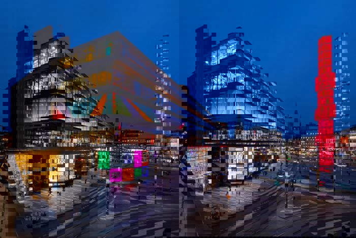 Kulturhusets fasad i kvällsljus med upplysta fönster och reklamskärmar i starka färger.