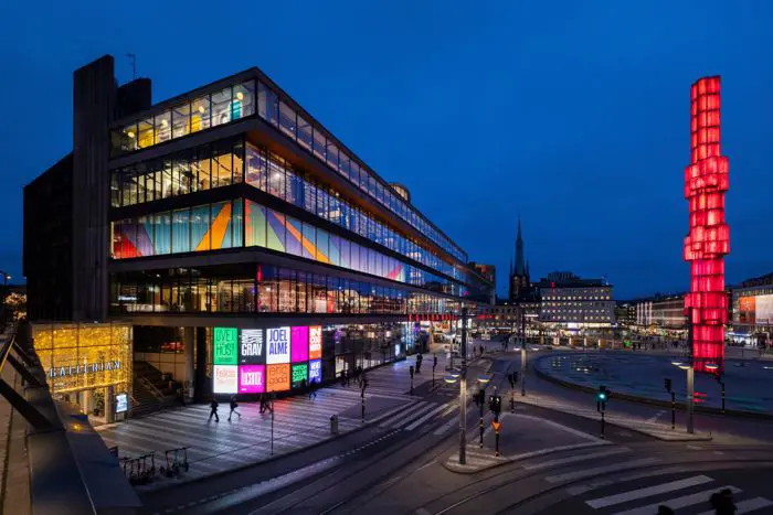 Kulturhusets fasad i kvällsljus med upplysta fönster och reklamskärmar i starka färger.