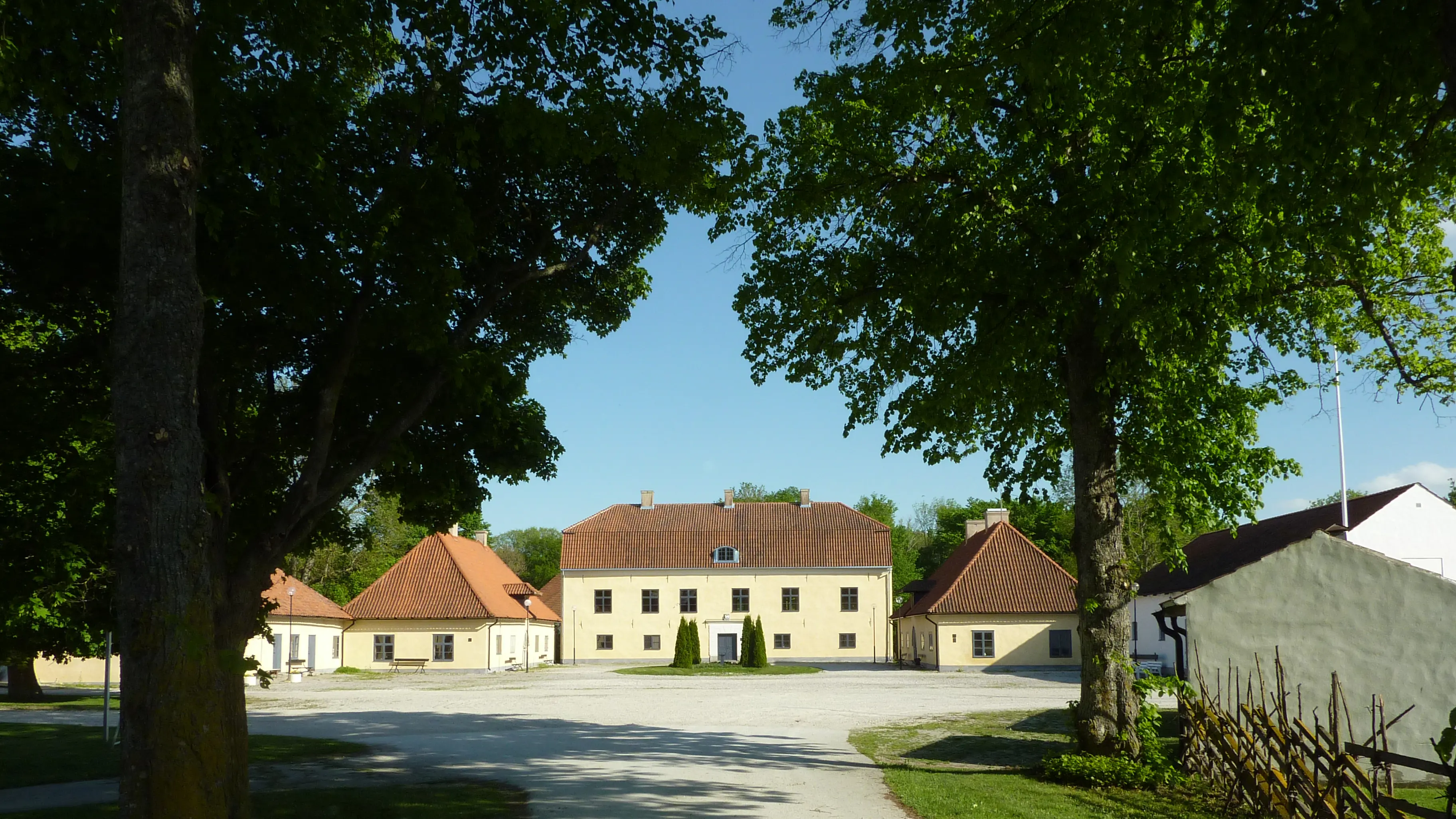 Roma kungsgård. Huvudbyggnaden med flyglar sedd från en av alléerna. Sommar och grönska.