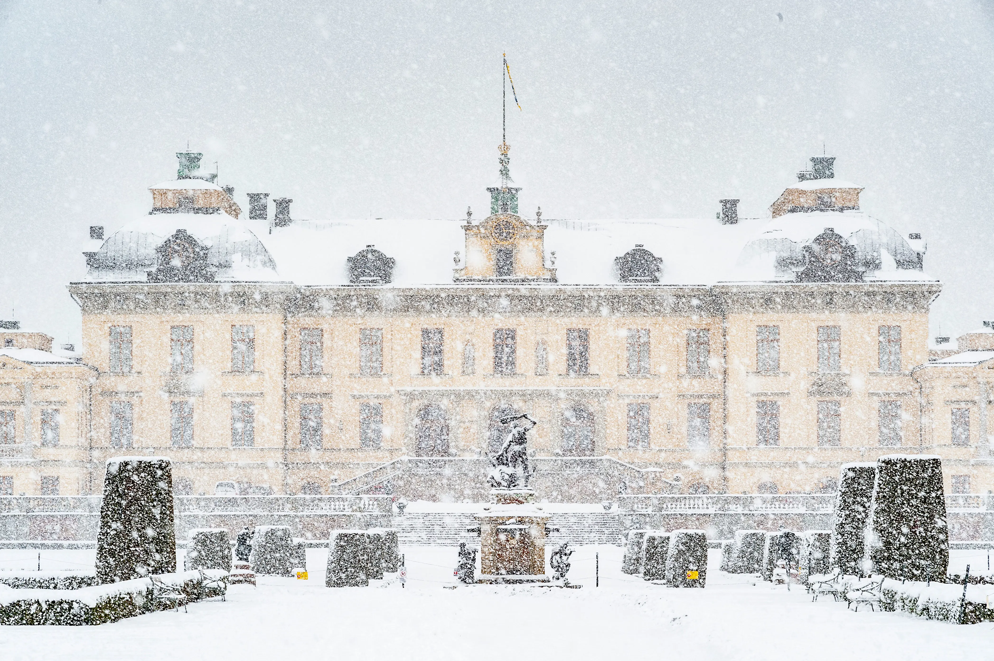 Slottet sett från parken på baksidan med en staty i mitten och snön som faller ner framför slottet.