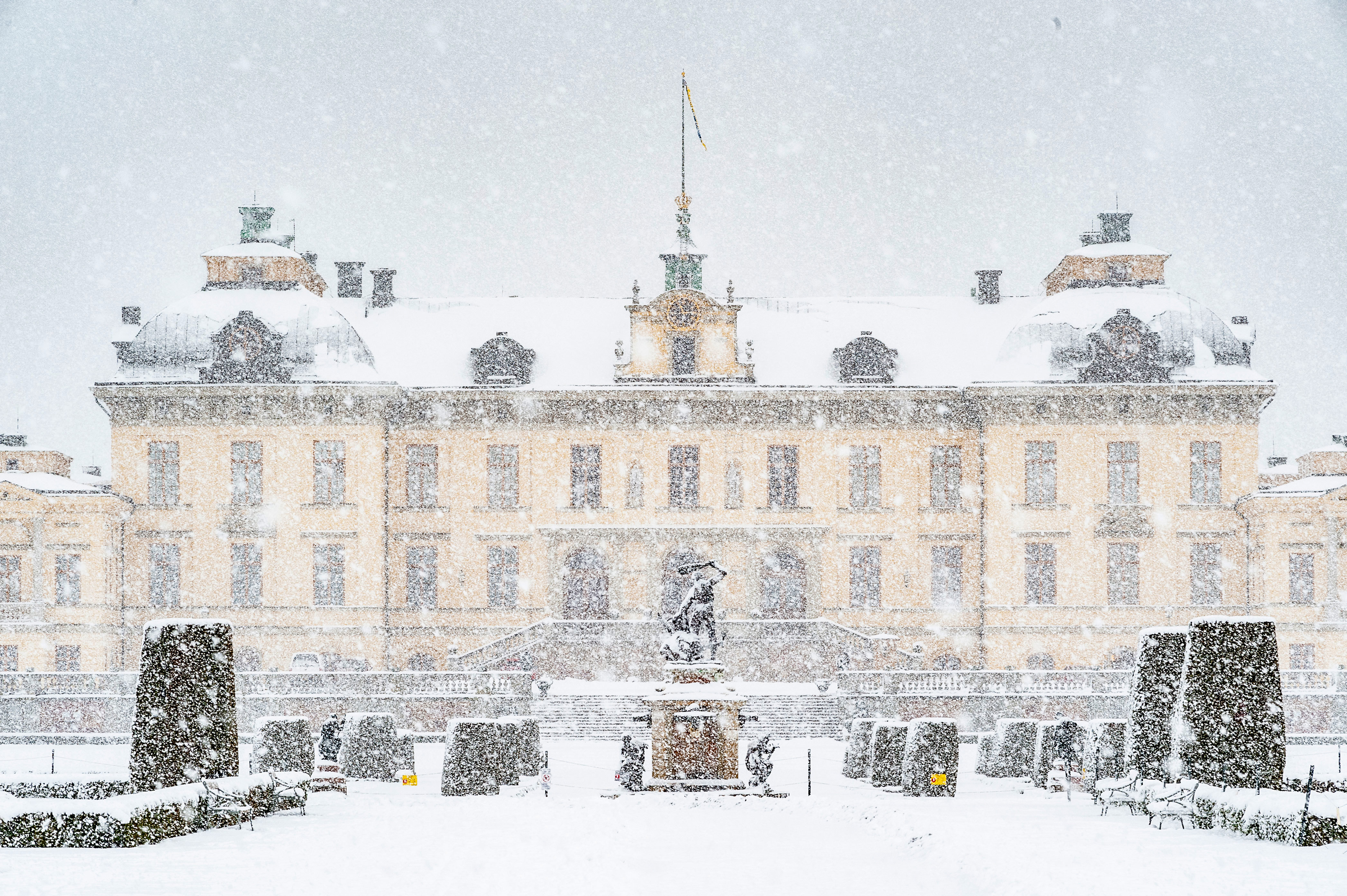 Slottet sett från parken på baksidan med en staty i mitten och snön som faller ner framför slottet.