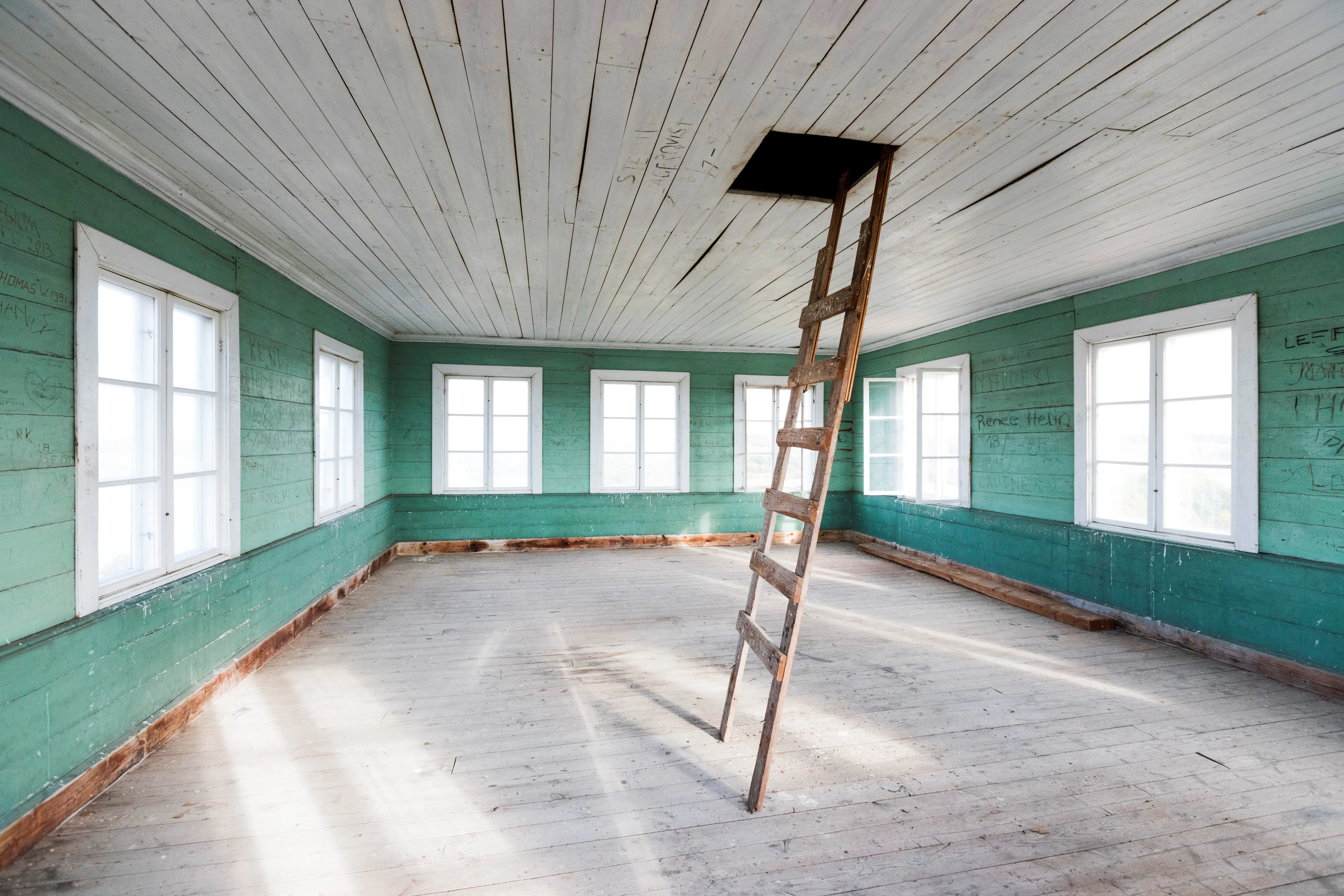 Interiör rum med plankväggar målat i grönt. Trägolv och fönster målade i vitt längs alla väggar. I mitten av rummet står en stege.