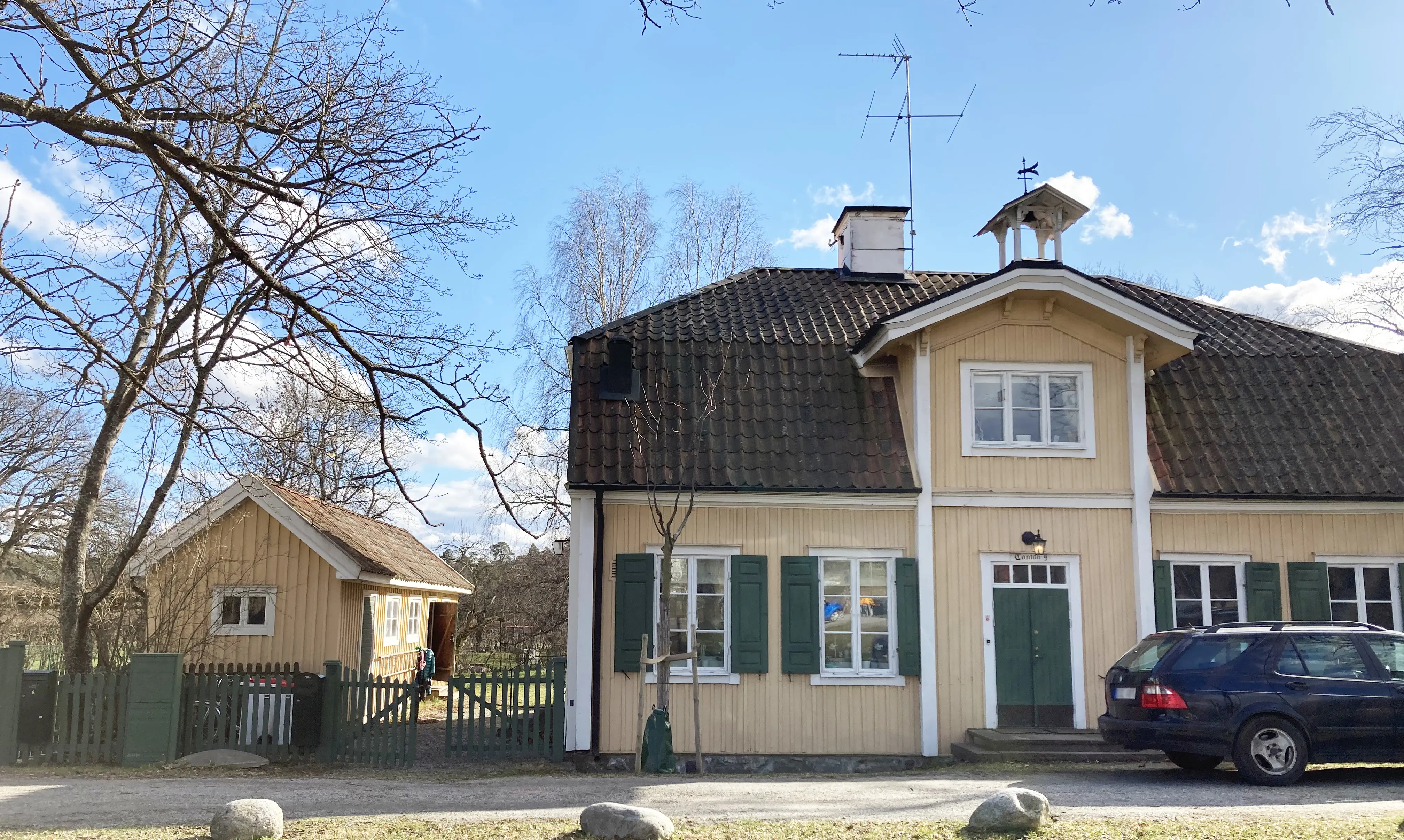 Kanton 9. Gult tvåvåningshus med gröna fönsterluckor och tegeltak. På taket ovanför porten sitter en liten klockstapel.