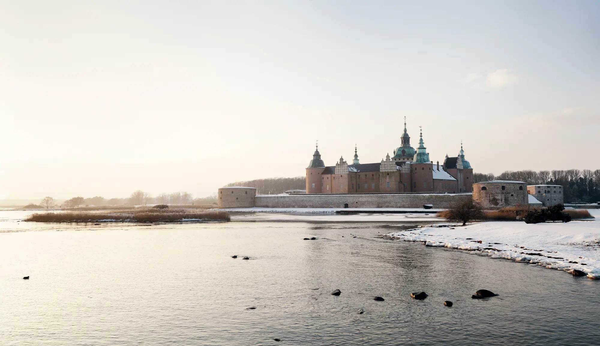 Kalmar slott med sina praktgavlar, torn och försvarsverk vid vattnet. Vinter, is, snö och dis.