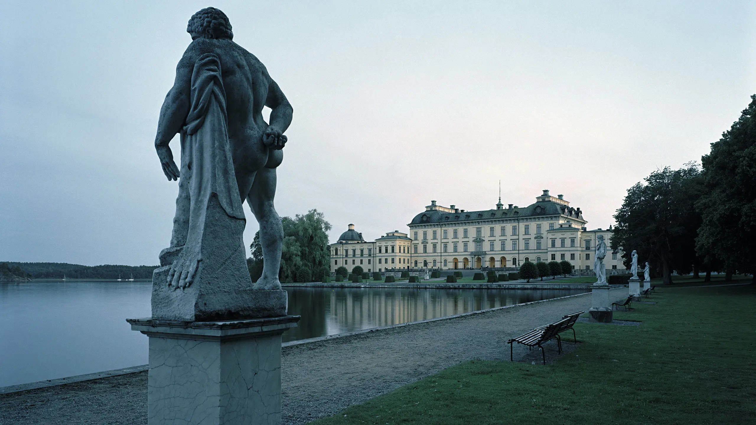 Drottningholms slott i skymningen med en skulptur i förgrunden.