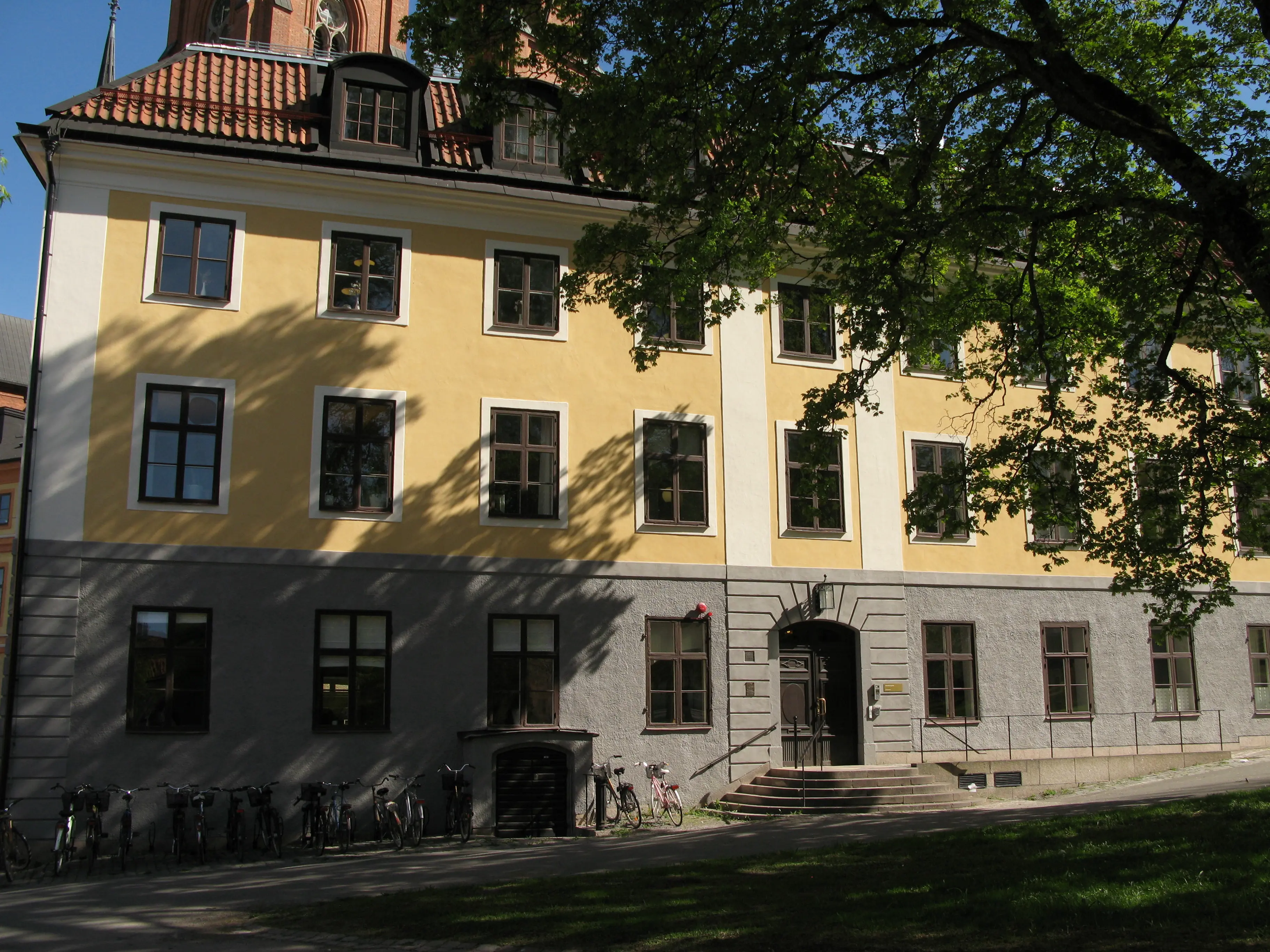 Ekermanska huset i Uppsala. Ett gulputsat trevåningshus med tak-kupor. Sommar och grönska.