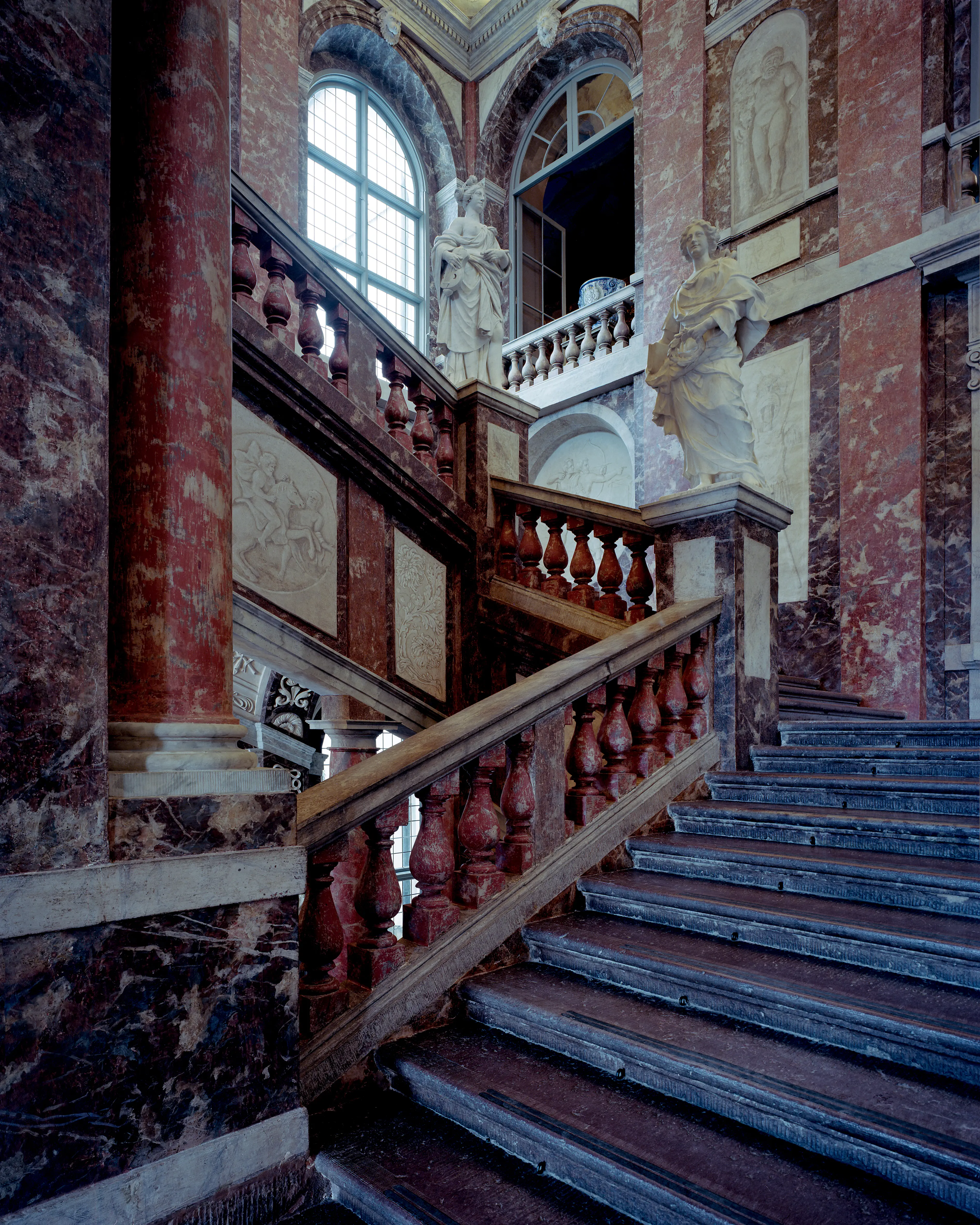 Stora trapp-hallen i Drottningholms slott. Väggarna är marmorerade i brunt och vitt. Den breda stentrappan har ett balustradräcke.