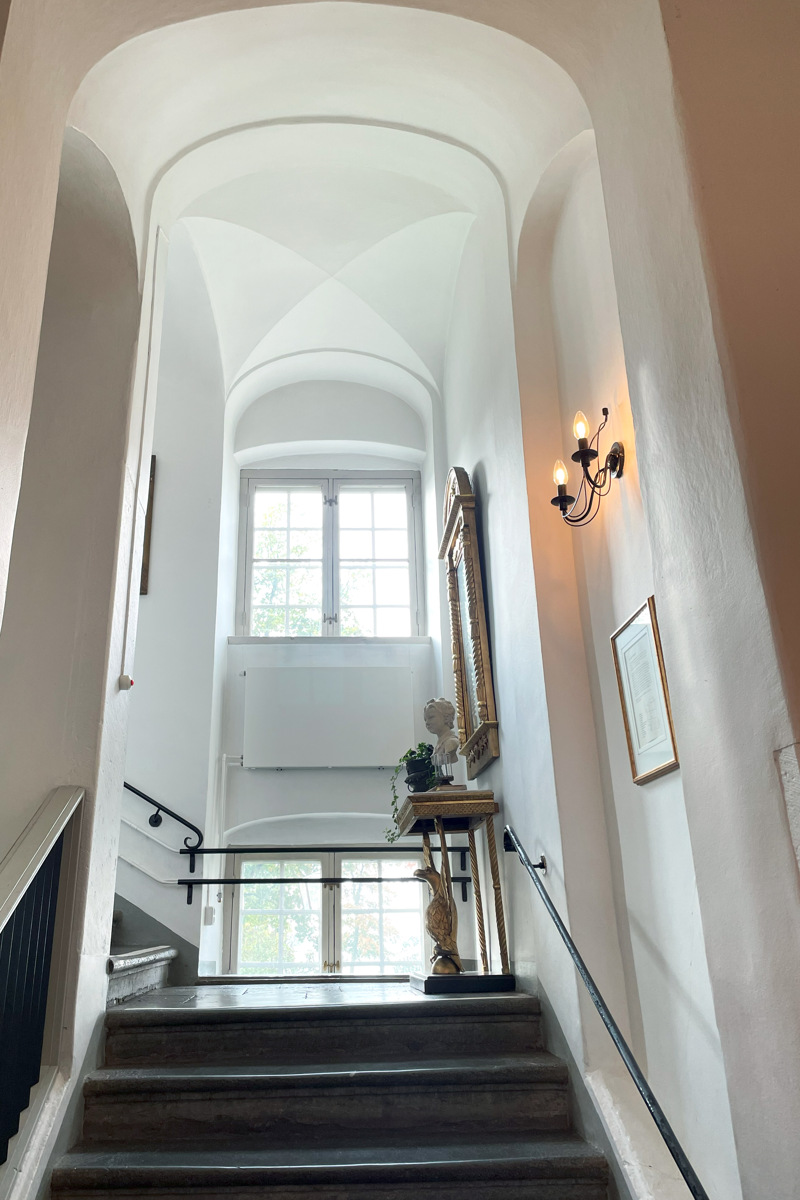 Trapphall i munkklostret. En stentrappa under ett högt och smalt valv med två fönster på höjden.