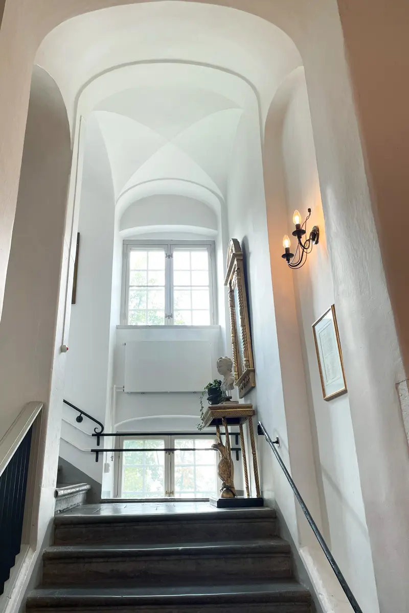 Trapphall i munkklostret. En stentrappa under ett högt och smalt valv med två fönster på höjden.