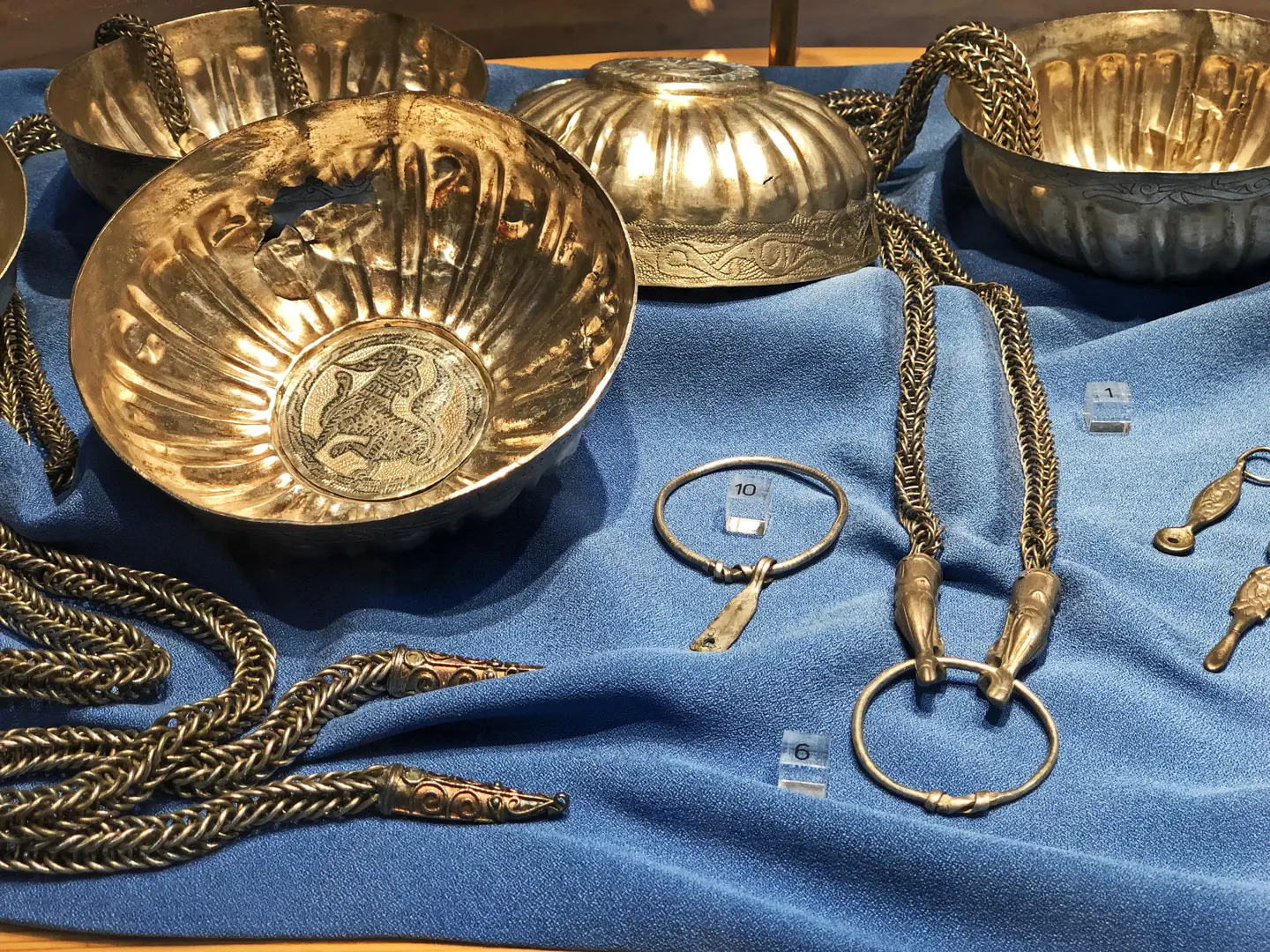 Gamla Uppsala museum. Monter med vikingatida guldföremål, bland annat tjocka länkar och skålar med filigranmönster.