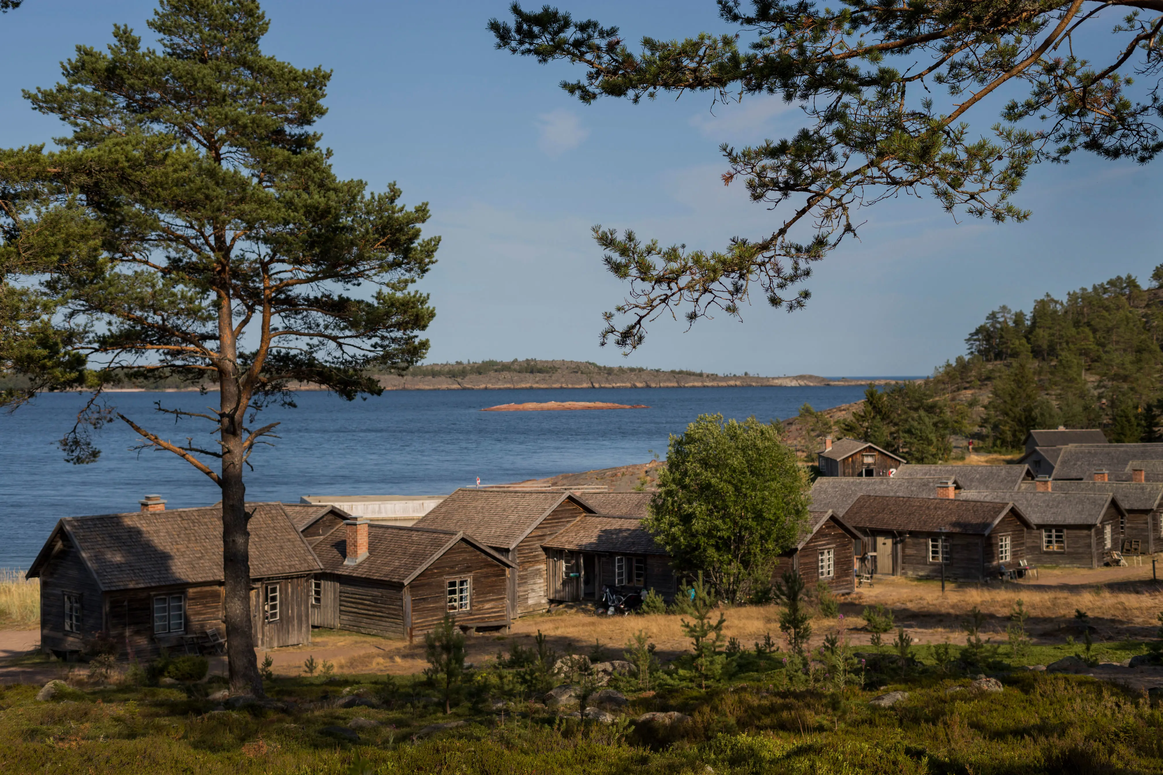 Blekta timmerhus på strand vid blått vatten.