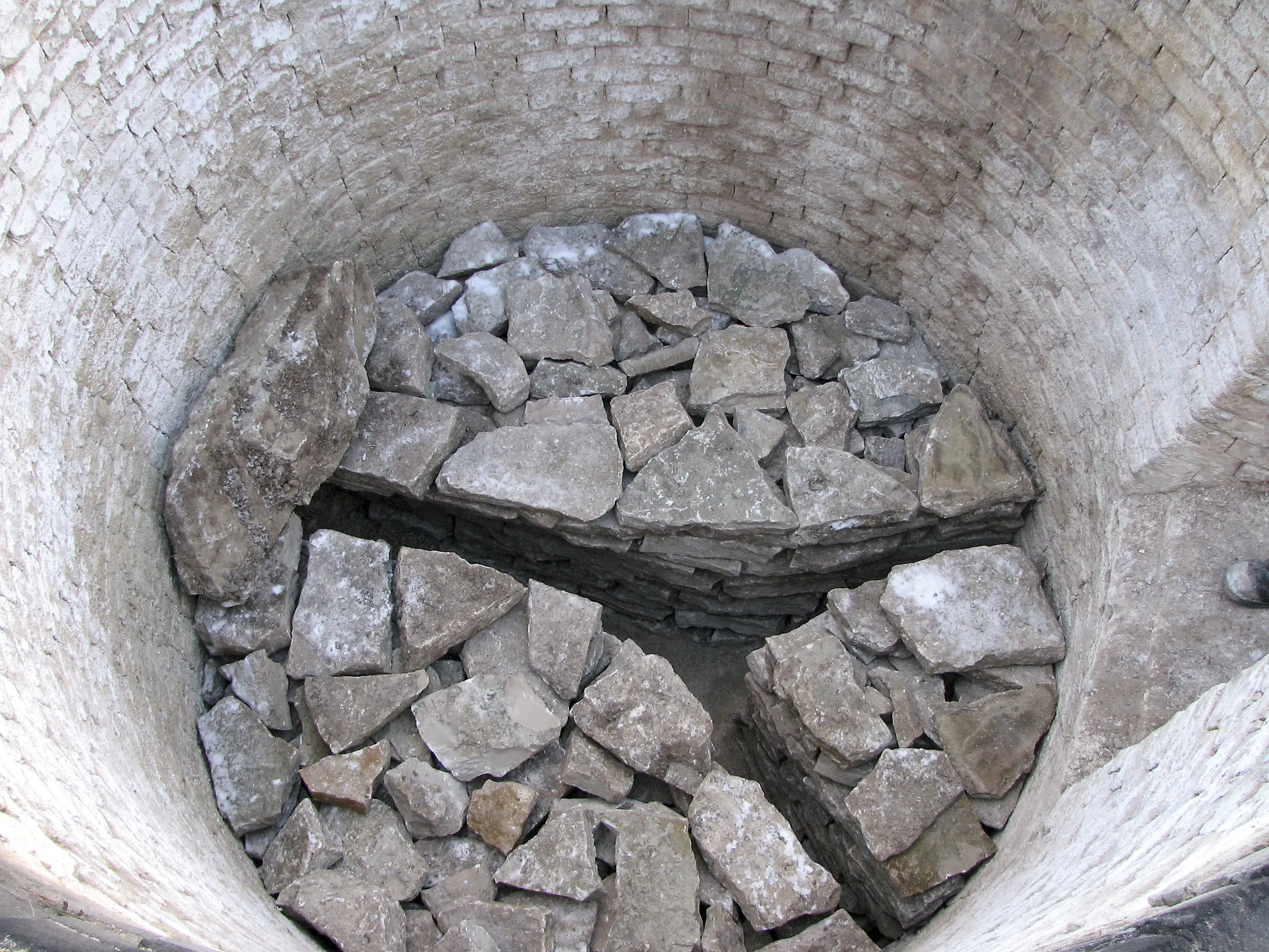 En rund murad brunn med grå, platta stenar i botten.