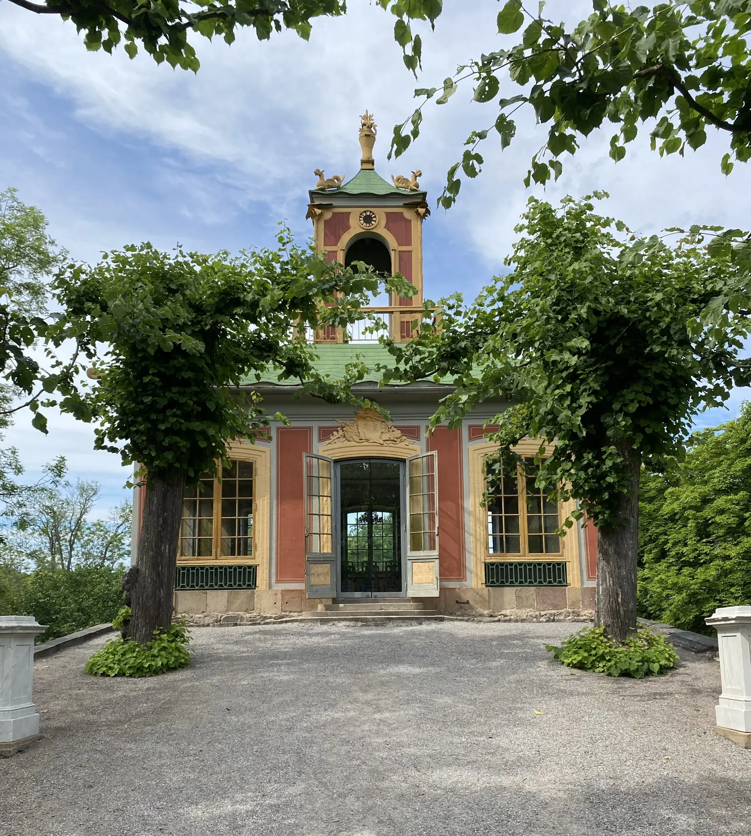 Confidencen vid Kina slott, Drottningholm. Röd liten paviljong med gula snickerier och ett torn på taket. Sommar och grönska.