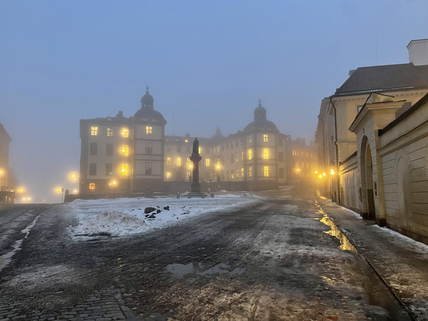 Wrangelska palatset en dimmig vinterkväll med snö på marken. Det lyser från palatsets fönster med ett gult sken.