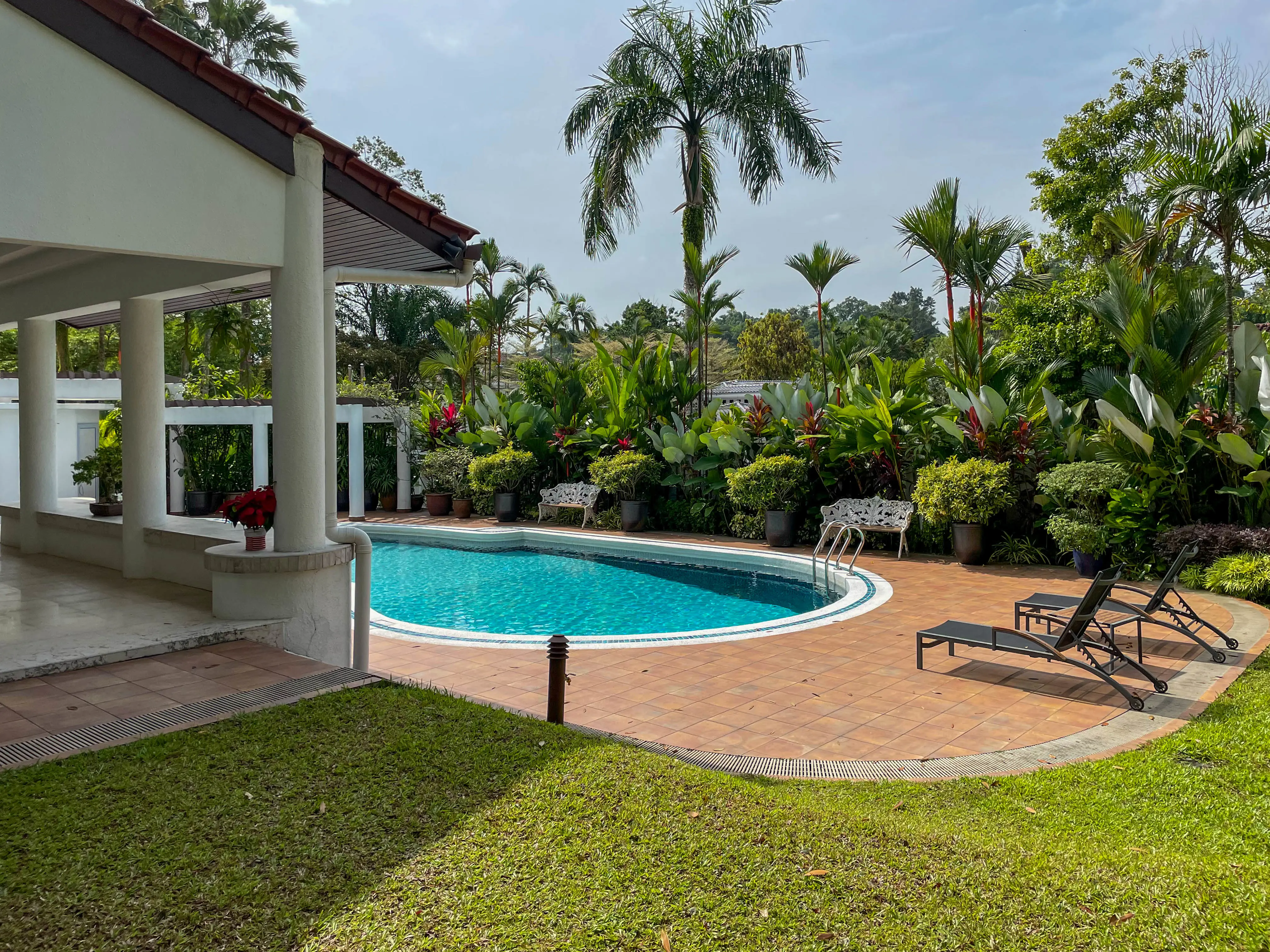 En vit villa med pelare till vänster, en pool och en stenlagd terrass