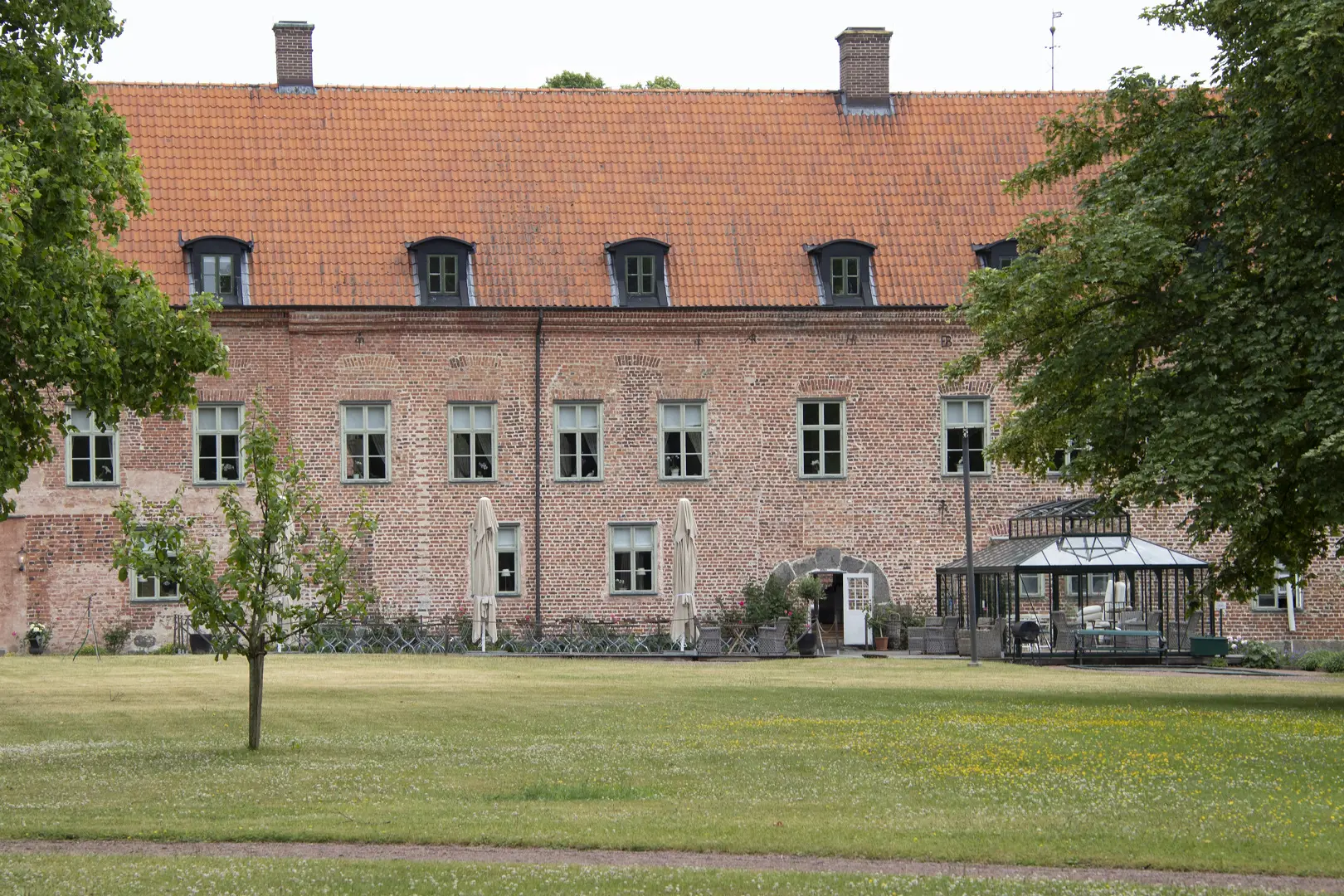 Slottets tegelfasad med en gräsmatta och lövträd i förgrunden.