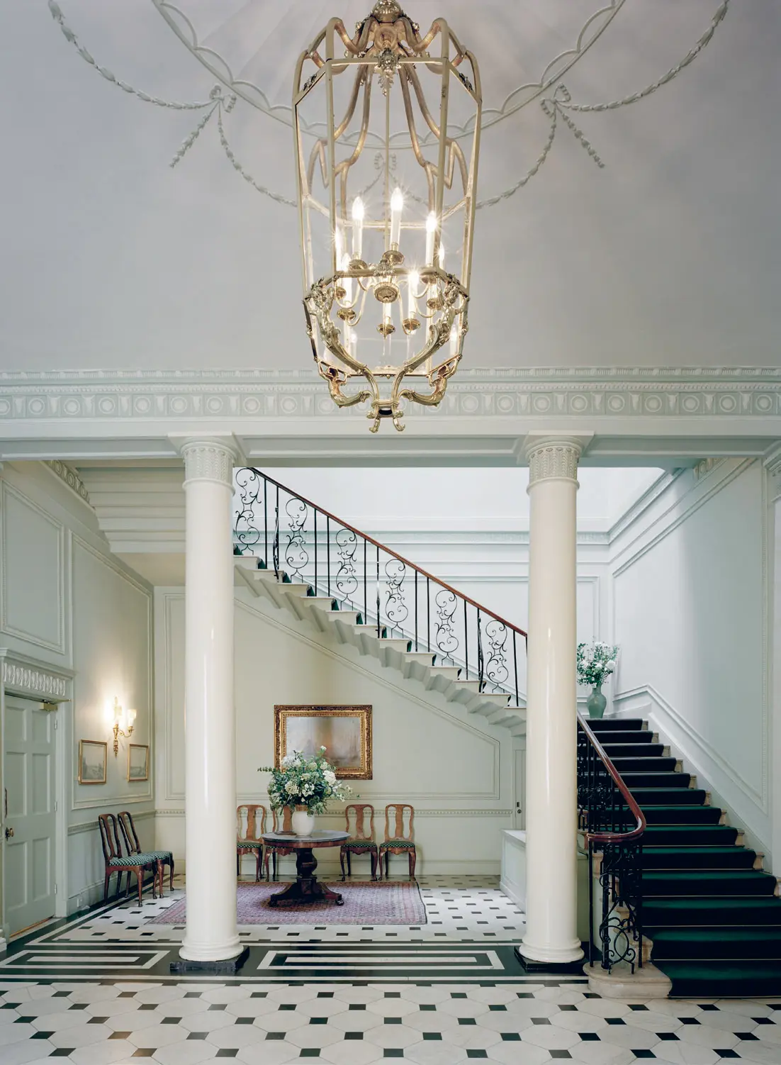 Interiör, ambassadresidenset i London. Hall med pelare, smidd tak-krona och svart- och vitt golv. Trappan har sirligt smidesräcke.