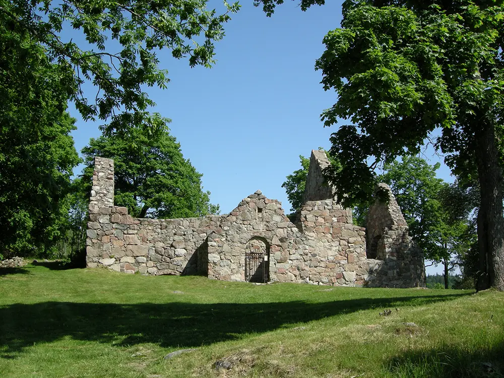 Kärnbo kyrkoruin. Stenmurarna till en liten medeltida kyrka. Sommar och grönska.