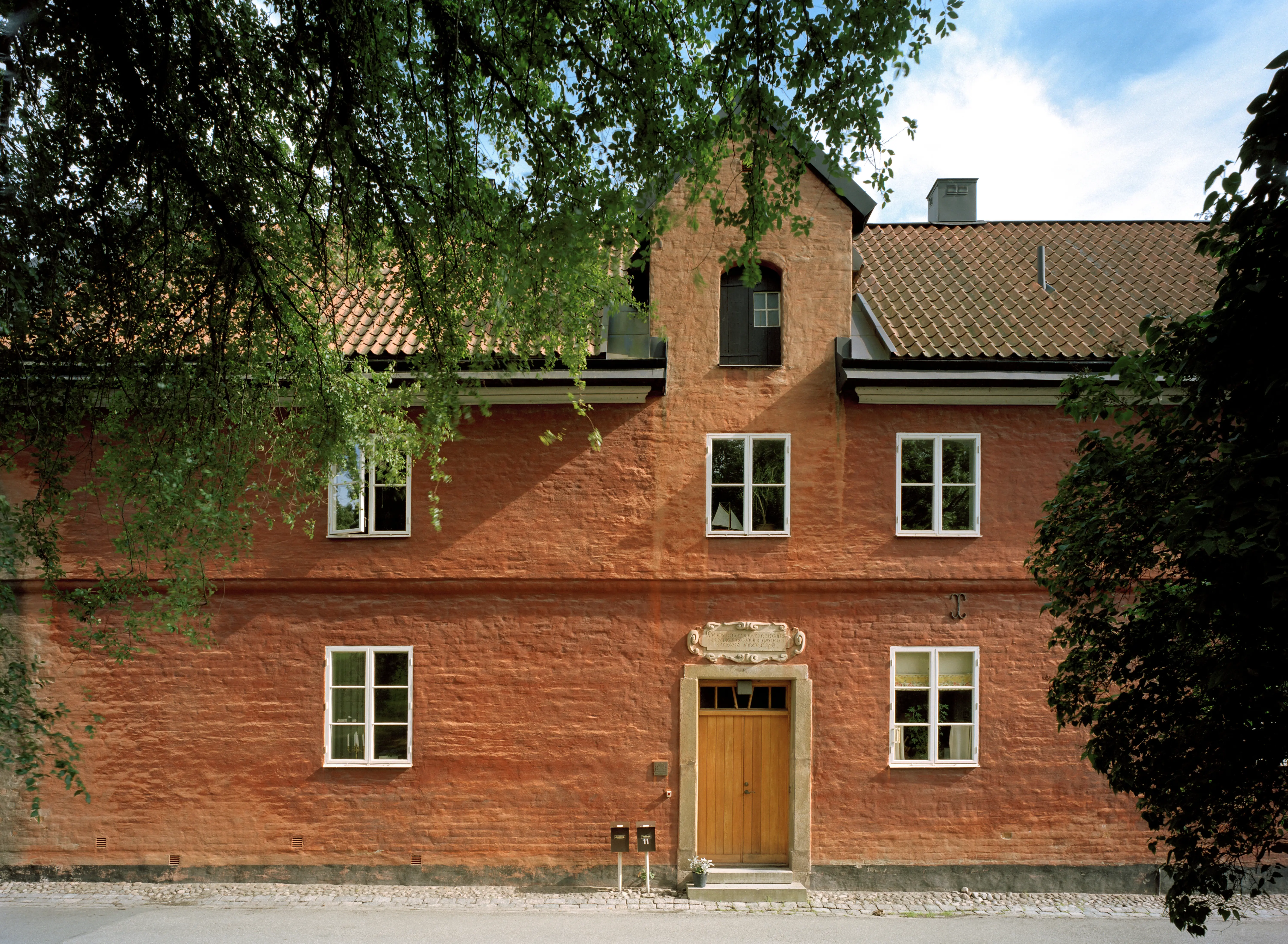 Paulinska gården. En rödputsad byggnad med tegeltak och stenportal mot gatan. Sommar och grönska.