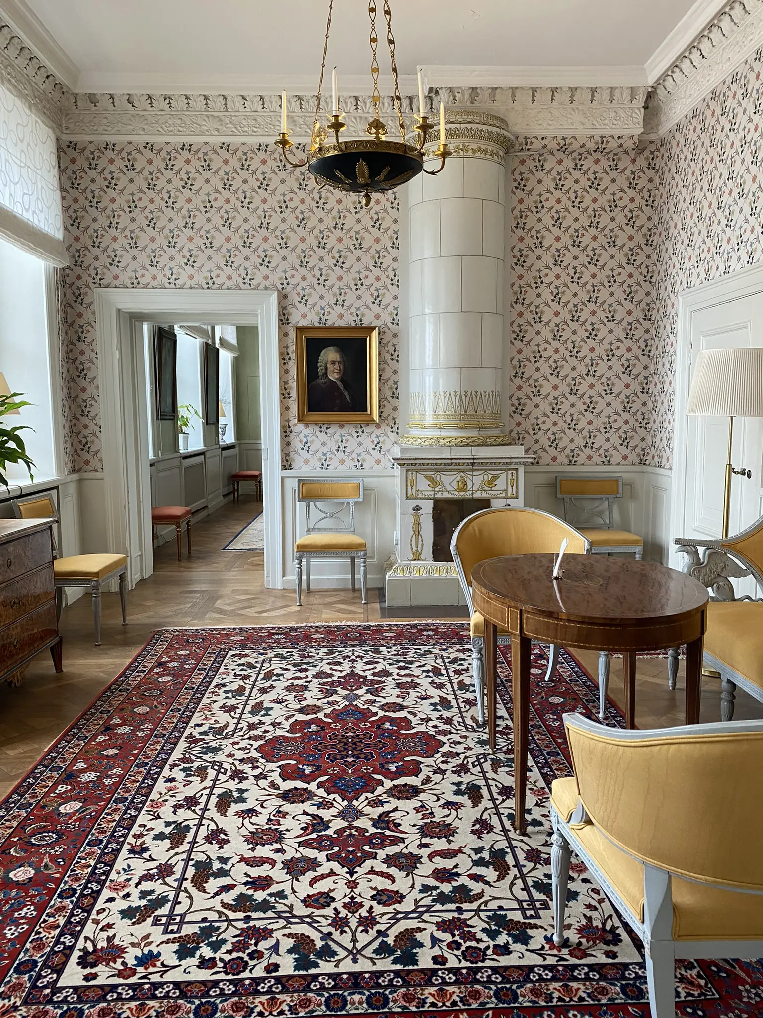 Tessinska palatset. Rum med småblommig tapet och stor äkta matta. Kakelugnen och de sidenklädda möblerna går i gult och vitt.